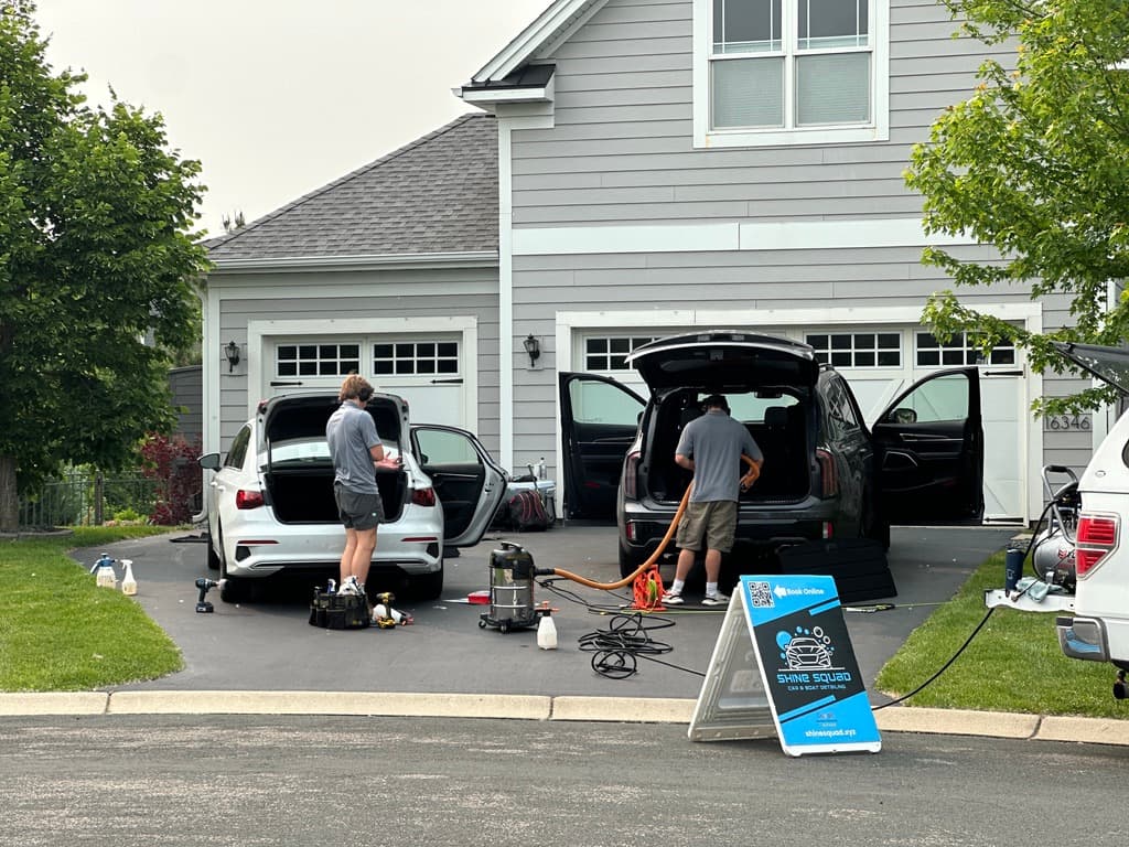 Two technicians detailing cars in a driveway for a local auto detailing business
