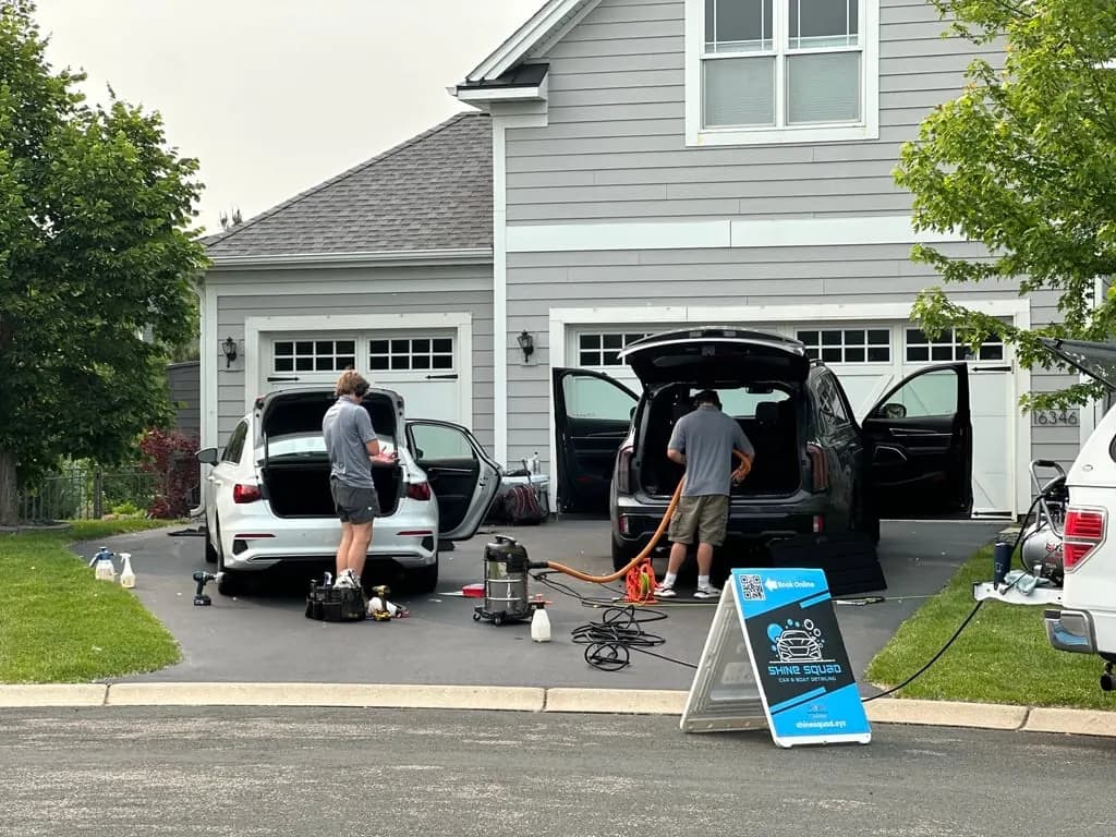 Two technicians detailing cars in a driveway for a local auto detailing business
