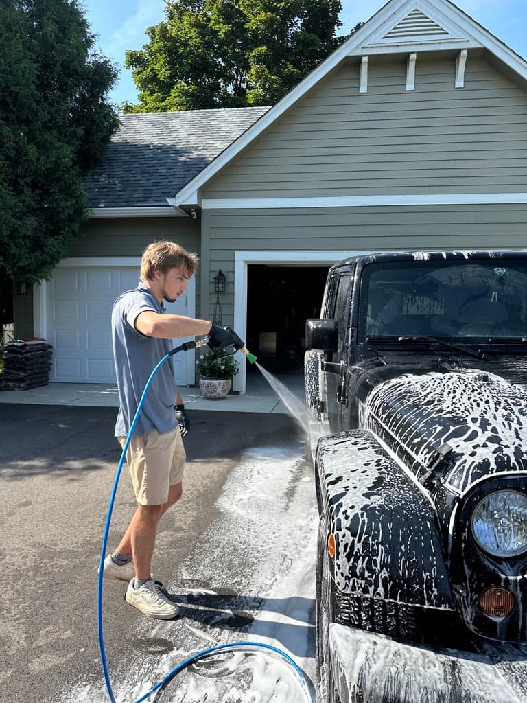 Mobile auto detailing technician foam-washing a vehicle in a driveway