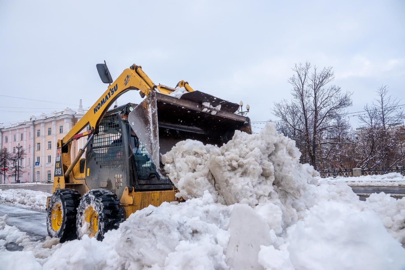 Skid-steer loader clearing a large pile of snow from a commercial lot